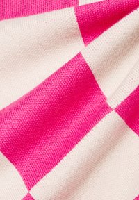 Tissu en coton tricoté avec un motif à carreaux alternant rose et crème, avec une surface texturée et des détails de couture visibles.