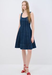 Denim A-line mekko, jossa on neliön muotoinen kaula-aukko, paksut hihnat ja kontrastiväriset ompeleet. Täydennetty punaisilla remmisandaaleilla.