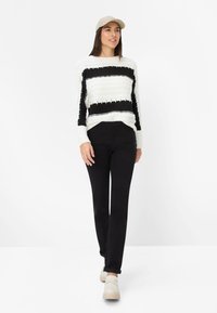 Hvid og sortstribet sweater med tekstureret design, sorte bukser og beige slip-on sko. Kombineret med en lysefarvet kasket.