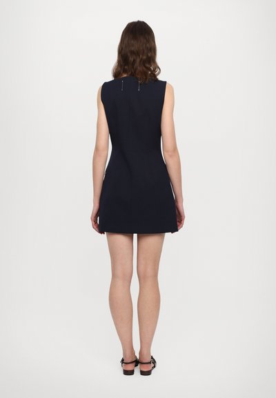 Rochie mini fără mâneci, bleumarin, cu o siluetă ajustată, textură netedă și fermoar la spate. Prezintă un design minimalistic și linii curate.