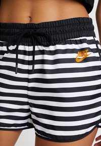 Black and white striped Nike shorts with an elastic waistband and drawstring. Features orange Nike logo on the left side. Made from smooth fabric.
