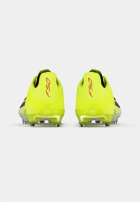 Κίτρινα ποδοσφαιρικά παπούτσια με αεροδυναμικό σχεδιασμό, επωνυμία F50 σε κόκκινο και διαφανές εξωτερικό πέλμα με ορατά καρφιά, από πίσω όψη.