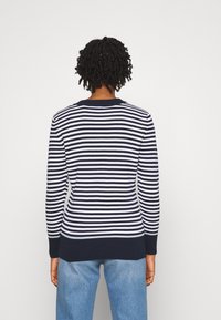 Pull en rayures bleu marine et blanc avec un col rond côtelé et des poignets, design ajusté et texture douce, associé à un jean bleu clair.