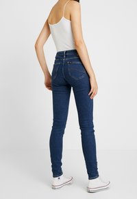 Smalblå jeans av denim med hög midja, fem fickor och kontrasterande sömmar, kombinerade med vita sneakers.