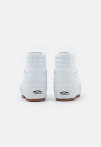 Zapatillas deportivas altas blancas con parte superior de lona texturizada, cuello acolchado y suela de goma; presenta una marca negra en el talón trasero.