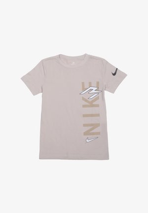 T-shirt beige à manches courtes de Nike avec un grand texte vertical "NIKE" et des logos swoosh sur la poitrine et la manche.