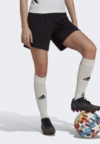 Black soccer shorts, white knee-high socks with black logo, and black cleats on a multicolored soccer ball, set against a light background.