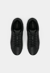 Adidași negri cu un exterior din piele netedă, vârful rotund și talpă din cauciuc alb. Au șireturi negre și un logo pe limba adidașilor.