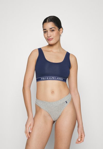 Navy blue crop top with a wide white logo band, paired with light gray thong underwear featuring a small navy logo. Stretch fabric, fitted design.