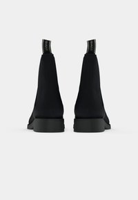 Paire de bottines noires avec languettes portant la mention "GANT", vues de dos sur un fond gris clair.