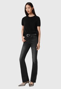 Zwart, donzig kort mouwen truitje, zwart high-waisted spijkerbroek met witte zijstiksels, en zilveren, metallic puntige schoenen.