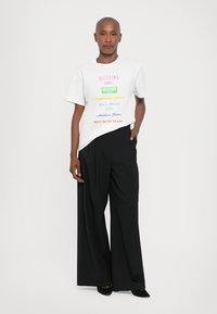 White t-shirt featuring multicolored text, paired with wide-leg black trousers and black shoes. Simple design, casual fit.