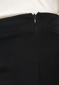 Μαύρη φούστα με κεντρικό, κλειστό μαύρο φερμουάρ στο πίσω μέρος, συνδυασμένη με ανοιχτό μπεζ τοπ.