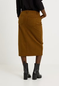 Jupe midi en velours côtelé marron avec deux poches arrière, portée avec des bottines noires à talons présentant une finition texturée et des bouts ronds.