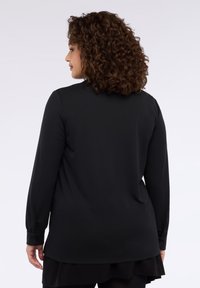 Czarna koszula z długim rękawem, okrągłym dekoltem i mankietami na guziki, o gładkiej fakturze i luźnym kroju, noszona na czarnej spódnicy.