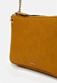 Borsa a tracolla in finta pelle gialla con texture, chiusura con zip, tracolla a catena e un piccolo logo del marchio embossato in basso a destra.