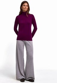 Long-sleeve purple turtleneck top paired with loose, gray wide-leg pants. Smooth texture and minimalistic design with no patterns.