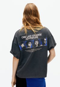 Tricou gri supradimensionat cu un design grafic format din patru portrete în rame albastre și textul „ONE LAST STRANGE ADVENTURE” pe spate.