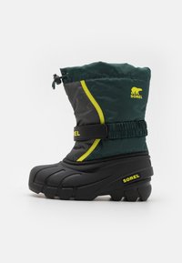 Bota de nieve impermeable en verde y negro, con parte superior de nailon, suela de goma, parte superior ajustable con cordón y acentos reflectantes en amarillo.