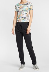 Grafisk t-shirt med flerfärgig textdesign, kombinerad med svarta joggerbyxor som har två framfickor och dragsko i midjan. Silverfärgade sneakers.