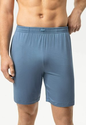 Man draagt eenvoudige blauwe shorts met elastische taille, getoond van midden torso tot midden dij op witte achtergrond.