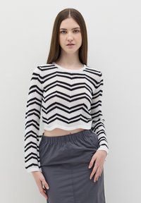 Maglione cropped a righe bianche e nere con un motivo a zigzag e maniche lunghe, abbinato a una gonna grigia con vita elastica.