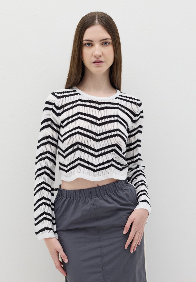 Maglione cropped a righe bianche e nere con un motivo a zigzag e maniche lunghe, abbinato a una gonna grigia con vita elastica.