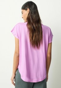 Kurzärmeliges, locker sitzendes Oberteil aus hellrosa Stoff. Verfügt über einen abgerundeten Saum und dezente Seitenschlitze, mit einer glatten, weichen Textur.