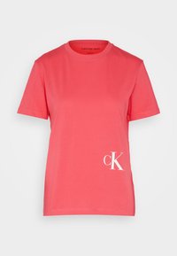Korálové tričko vyrobené z bavlny, s klasickým kulatým výstřihem, krátkými rukávy a bílým logem "ck" na dolní levé straně.