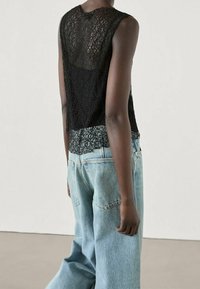 Un débardeur en dentelle noire présente un design texturé, associé à un jean en denim bleu clair, affichant une coupe ample et un style droit.