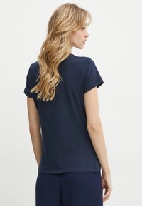 T-shirt a maniche corte di colore blu navy, realizzata in tessuto morbido, con collo a giro. Design semplice, vista posteriore che mostra una texture liscia e linee pulite.