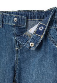 Jeans de denim con un lavado azul claro, que presentan una amplia cinturilla elástica, botón a presión plateado y costuras en amarillo contrastante.