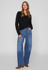 Svart stickad tröja med V-hals, kombinerad med ljusblå vida jeans. Bruna klackboots kompletterar outfiten. Enkelt mönster, avslappnad look.