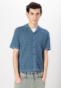 Short-sleeve button-up shirt in textured blue fabric with wavy pattern. Features a collared neckline and a straight hem.