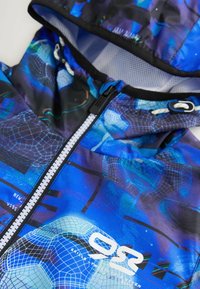 Giacca con cappuccio blu caratterizzata da un motivo geometrico, cerniera frontale e logo. Realizzata in tessuto leggero e testurizzato con dettagli neri.