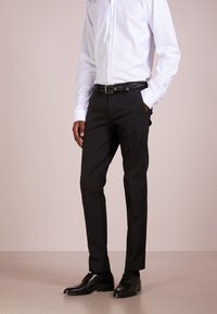 Sorte dressbukser med skreddersydd passform, flat front, sidelommer, sammen med en hvit skjorte med lange ermer og svarte skinnsko. teksturert belte.