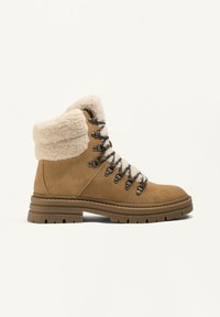 Barna velúr túracipő, műszőrme mandzsettával, fűzős előrésszel és masszív gumitalppal, amely mély barázdákkal rendelkezik a tapadás érdekében.