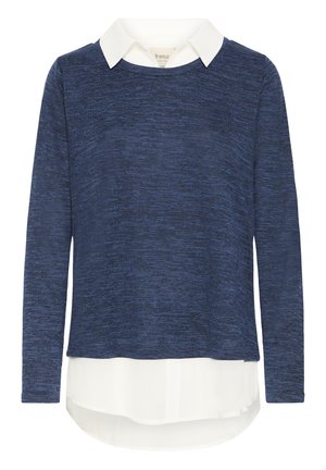 Marineblå langærmet sweater lagdelt over en hvid skjorte med krave og en buet kant, der rækker længere ned end sweateren.