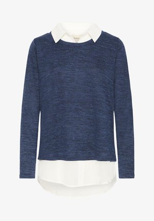 Granatowy sweter z długim rękawem nałożony na białą koszulę z kołnierzykiem, której zakrzywiony dół wystaje spod swetra.