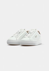 Sneaker bianche in pelle con una texture liscia, allacciatura frontale e dettagli beige sul tallone. Suola in gomma robusta con un design minimalista.