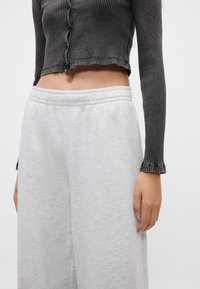 Ριχτή, σκούρα γκρίζα κοντή μπλούζα με κουμπιά και ξέφτια στο τελείωμα, συνδυασμένη με ανοιχτό γκρίζες, χαλαρές φόρμες με ελαστική μέση.