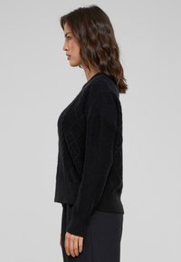 Zwarte trui met ruitpatroon, gemaakt van zacht materiaal, met lange mouwen en een iets cropped pasvorm.