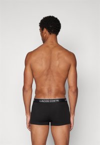 Svarte boxershorts med en myk livlinning som har logoen "LACOSTE" i hvitt. Stoffet ser glatt og elastisk ut.
