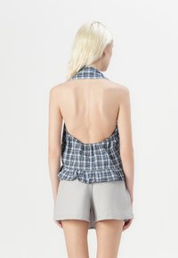 Blue and white plaid halter top with an open back, featuring a frilled hem and paired with light gray shorts. Smooth fabric texture.