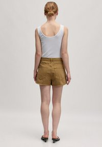 Bruine denim short met een rafelige zoom, eenvoudige achterzakken en een elastische tailleband, gecombineerd met een witte aansluitende tanktop.