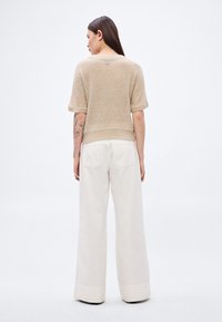 Šviesiai rudas megztinis trumpomis rankovėmis, trumpesnio kirpimo. Derinamas su platėjančiomis baltomis kelnėmis, kurių apačioje yra sulankstyta detalė.