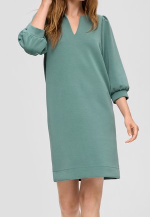 Grøn knælængde kjole med V-hals, løse 3/4 pufærmer, lavet af blødt stof, med minimalistisk design og afslappet pasform.