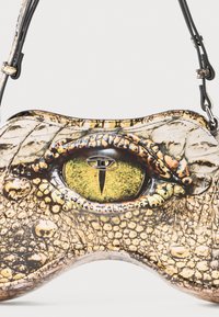 Crocodile-patterned handbag in textured materials, featuring a prominent yellow eye detail and black strap. Unique shape with glossy finish.