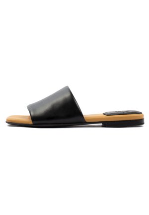 Black leather slide sandal with a wide strap and a tan rubber sole. Flat design with minimal hardware and a smooth texture.