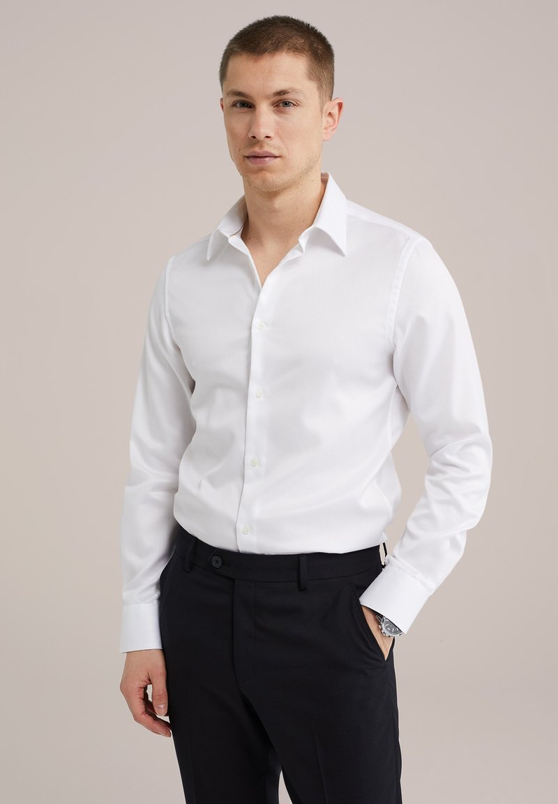 Camisa blanca de manga larga con cuello clásico y botón al frente, combinada con pantalones oscuros, destacando una textura suave y un diseño entallado.